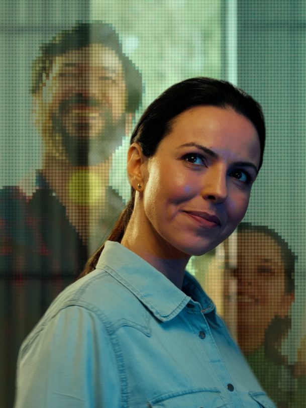 Mulher sorrindo diante de projeção de pessoas em pixels, cena de branded content