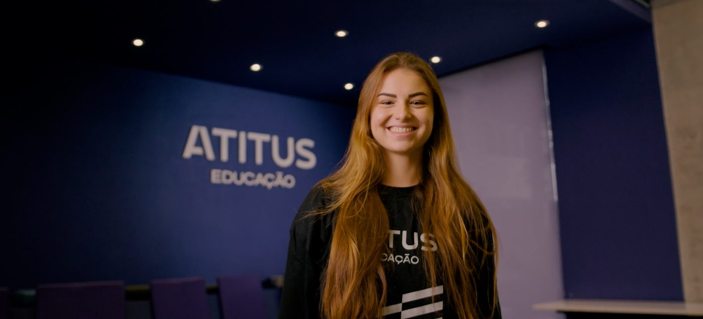 Estudante sorrindo em sala com a marca Atitus Educação ao fundo