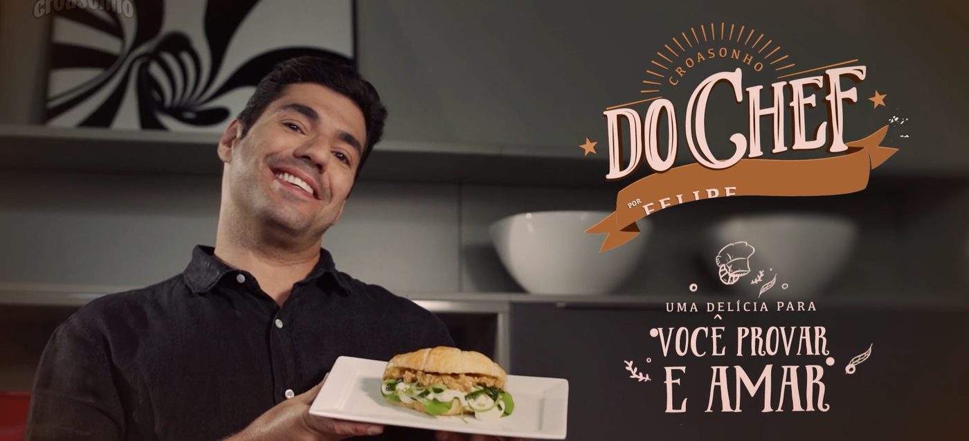 Chef apresentando sanduíche de croissant com letreiro ilustrado ao lado