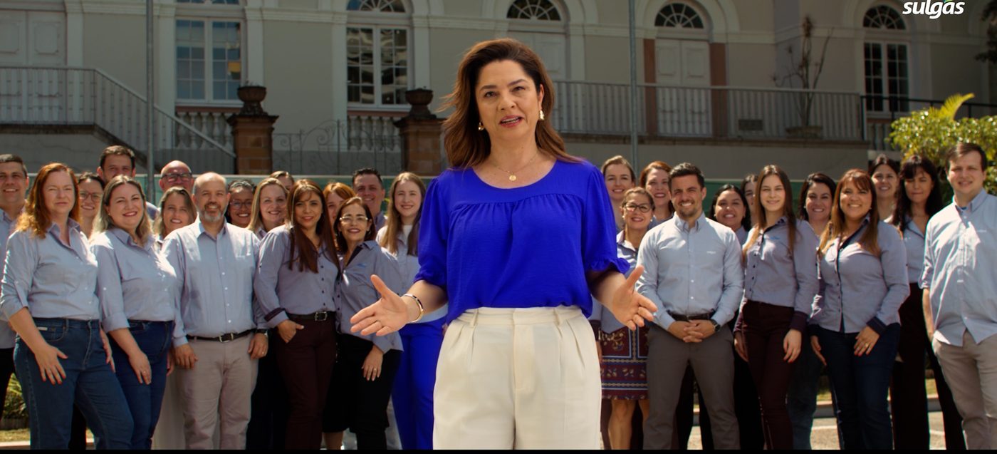 Executiva falando à câmera à frente da equipe da Sulgás em prédio histórico