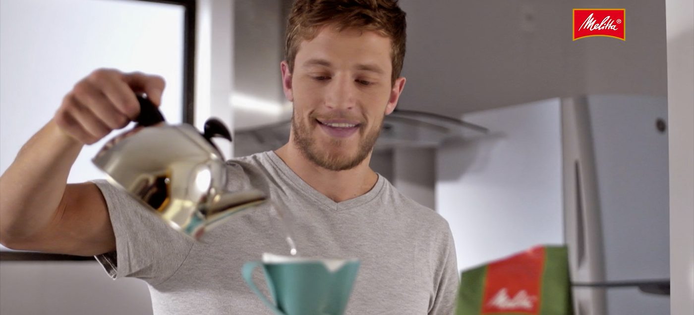 Homem passando café no filtro em cozinha, cena de comercial Melitta
