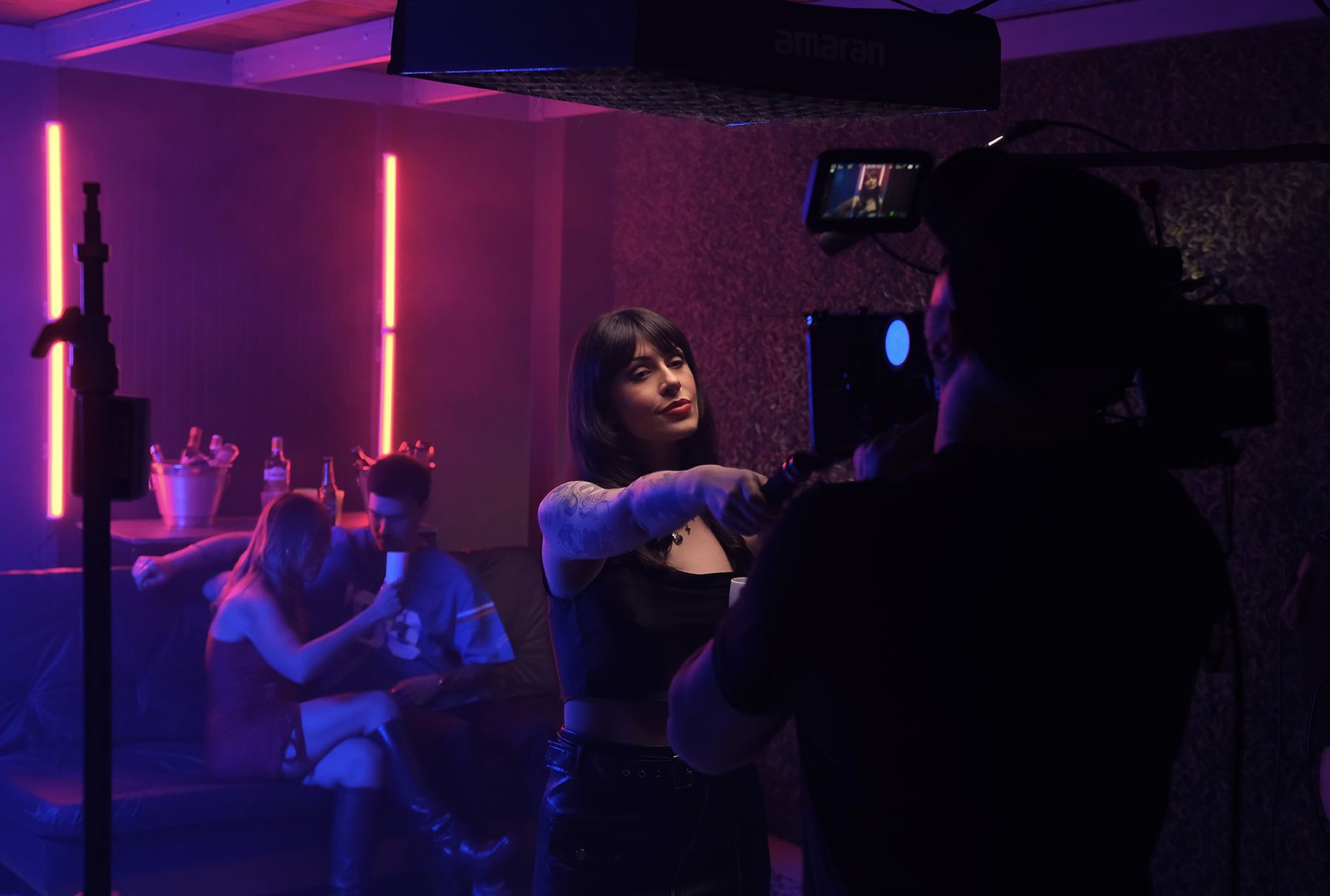 Cenário montado no estúdio com luzes neon roxas e elenco em cena durante gravação