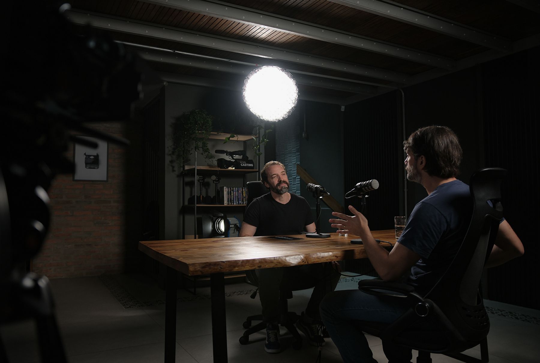 Gravação de podcast com dois convidados à mesa de madeira sob luz suave