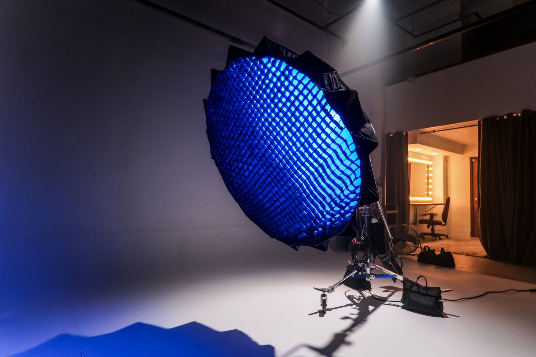 Refletor parabólico com grade e luz azul no fundo infinito, camarim iluminado ao fundo