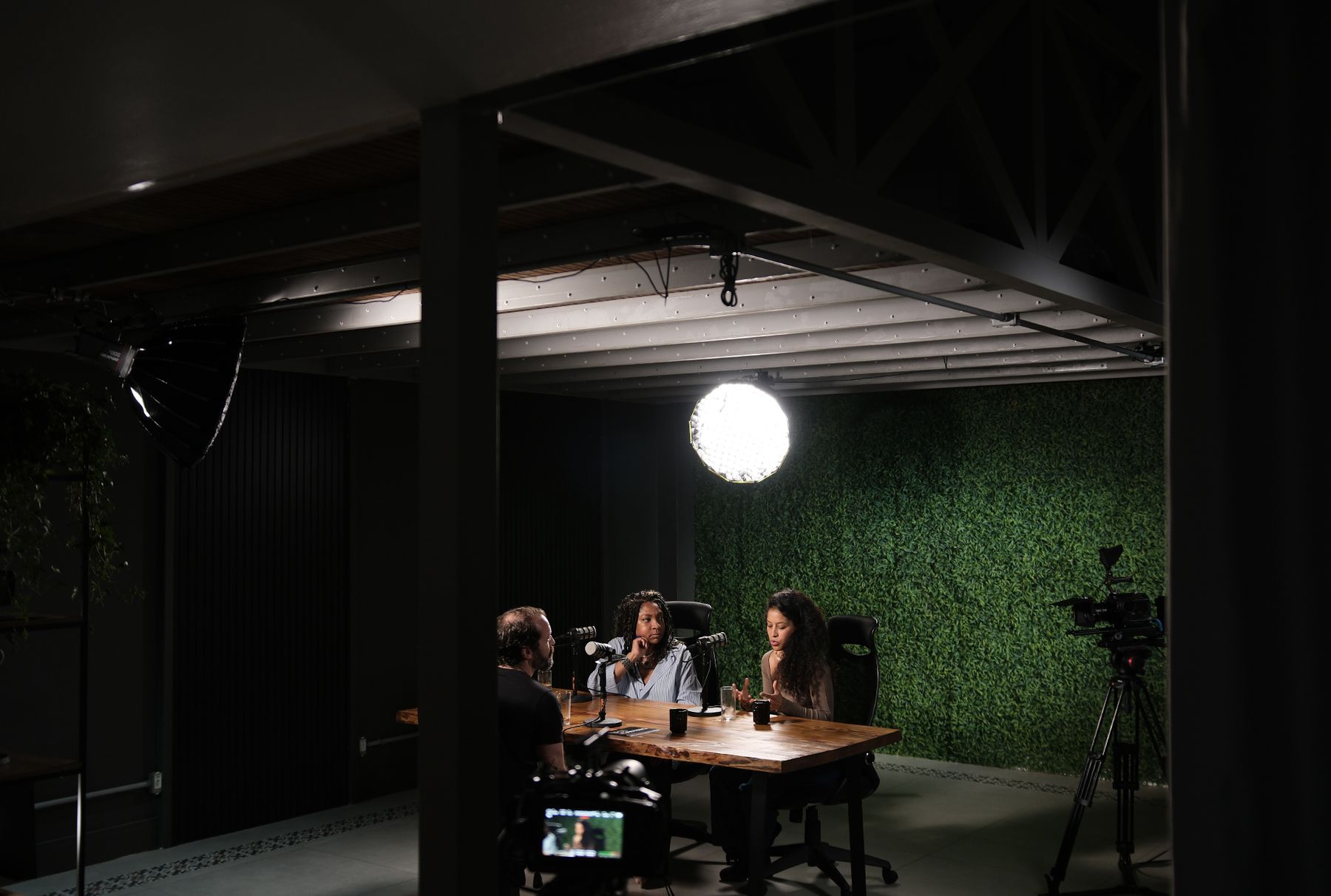 Videocast com três participantes em frente à parede verde, câmera em tripé ao lado