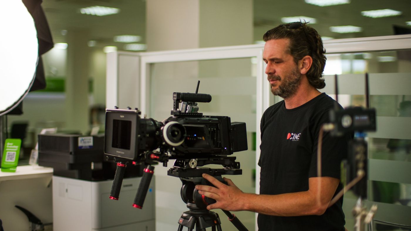 Operador da Cinematográfica com câmera de cinema em tripé gravando em escritório