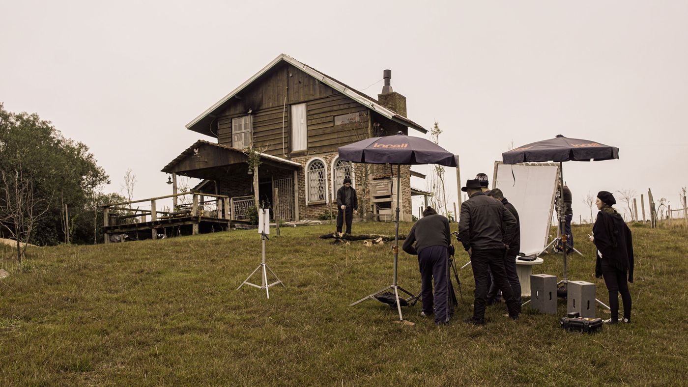Equipe montando set com rebatedores e guarda-sóis em frente a casa de madeira no campo