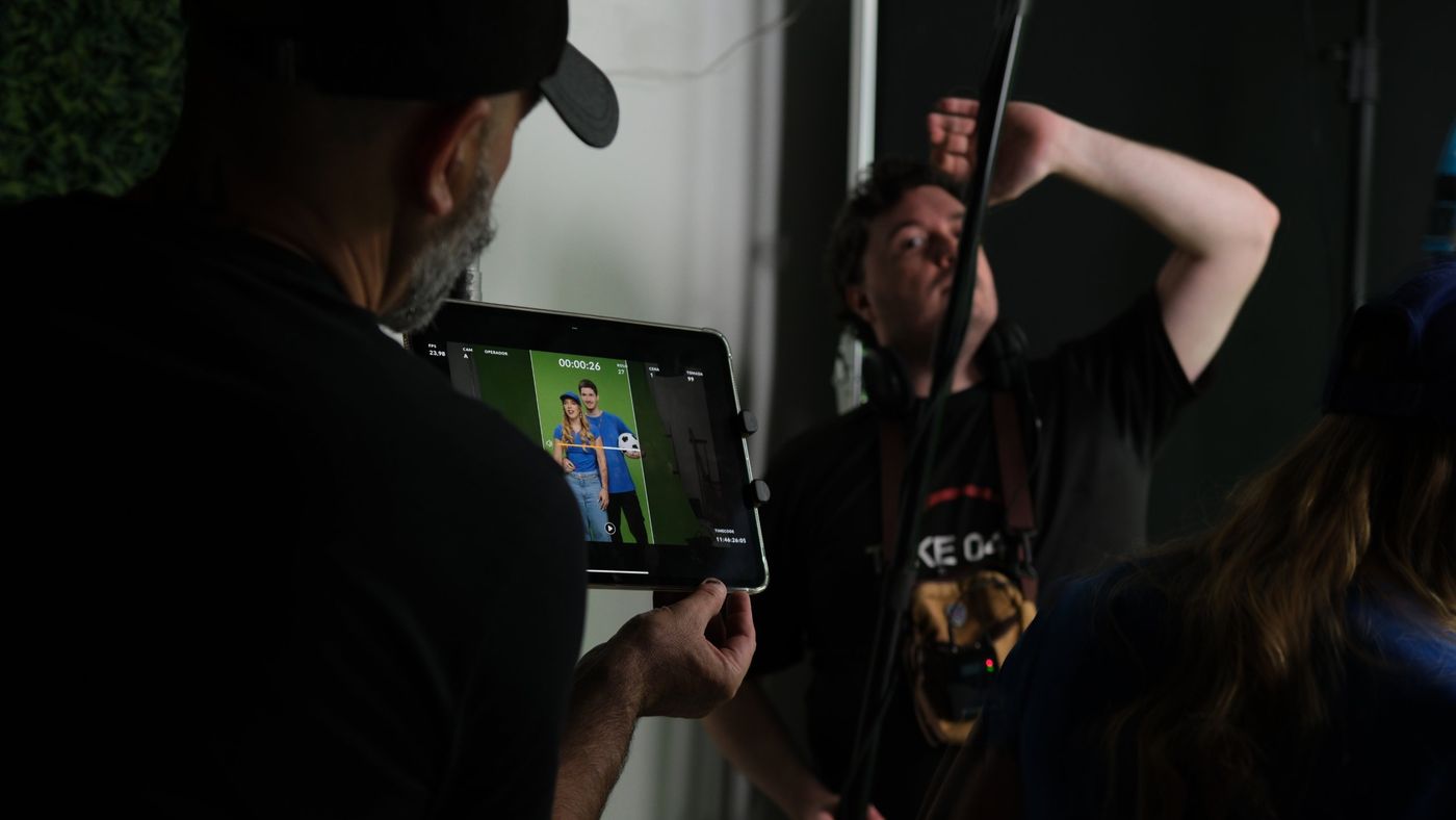 Diretor revisando take no tablet enquanto técnico de som ajusta o boom no set