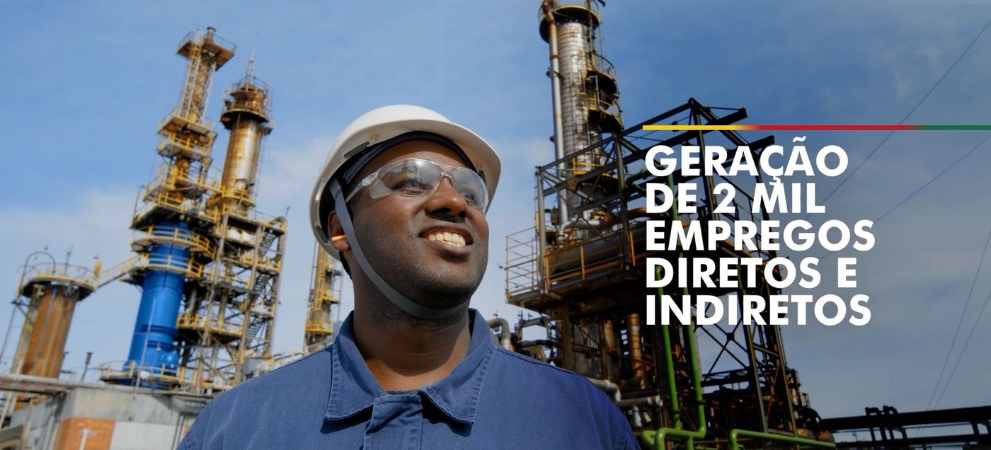 Trabalhador de capacete sorrindo em frente a uma refinaria, com texto sobre geração de empregos