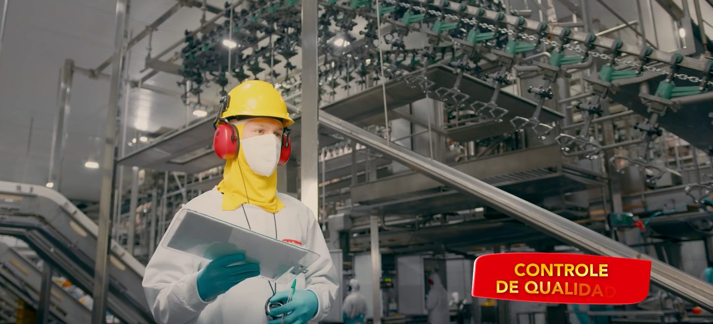Colaborador com EPI fazendo controle de qualidade em linha de produção de indústria alimentícia